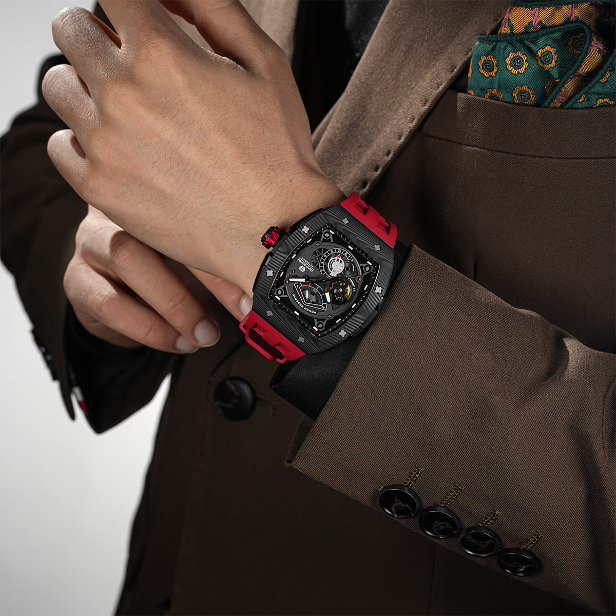 Close-up of a model wearing the TSAR BOMBA Elemental TB8210CF Passion Red men’s tonneau watch, featuring a tonneau stainless steel case, a carbon fiber bezel, and red strap. The Seiko Epson automatic movement is displayed with a tourbillon at 9 o’clock, a power reserve indicator at 12 o’clock, and a 24-hour display at 6 o’clock.